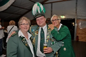 Traditionelle Schützenbrüder in grünen Uniformen bei Festivitäten, mit einer Person in Zylindermütze und zahlreichen Abzeichen, in einer festlichen Umgebung.
