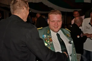 Hochwertiger Mann in Uniform mit Orden bei einem Schützenfest, lächelnd im Gespräch.