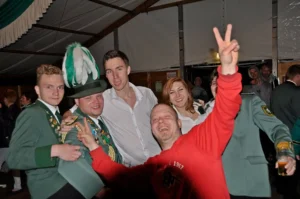 Fröhliche Gruppe von Schützenbrüdern bei einem Fest in Köln, mit einem Mann in historischen Uniformen und traditionellen Hüten, die gemeinsam feiern und Spaß haben.