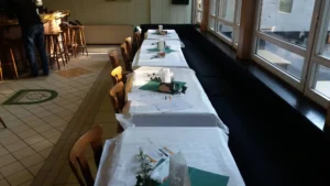 Reihe von Tischen in einem Restaurant, gedeckt mit weißen Tischdecken und grünen Servietten.