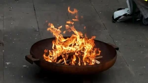 Feuerstelle mit lodernden Flammen und Holzscheiten in einem runden Metallbehälter.