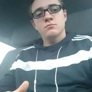 Junger Mann mit Brille, der in einem Auto sitzt und einen Daumen hoch zeigt.